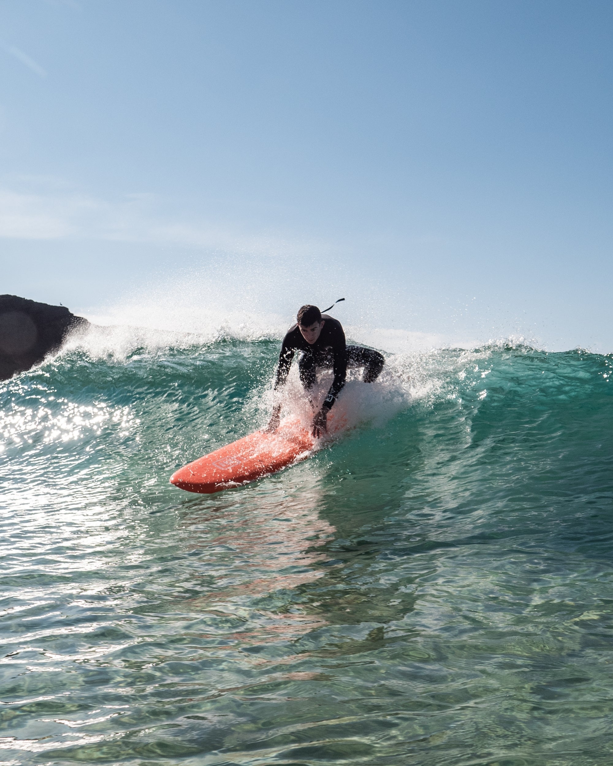 Orange 7'6 surfboard on water with rider crouched on wave