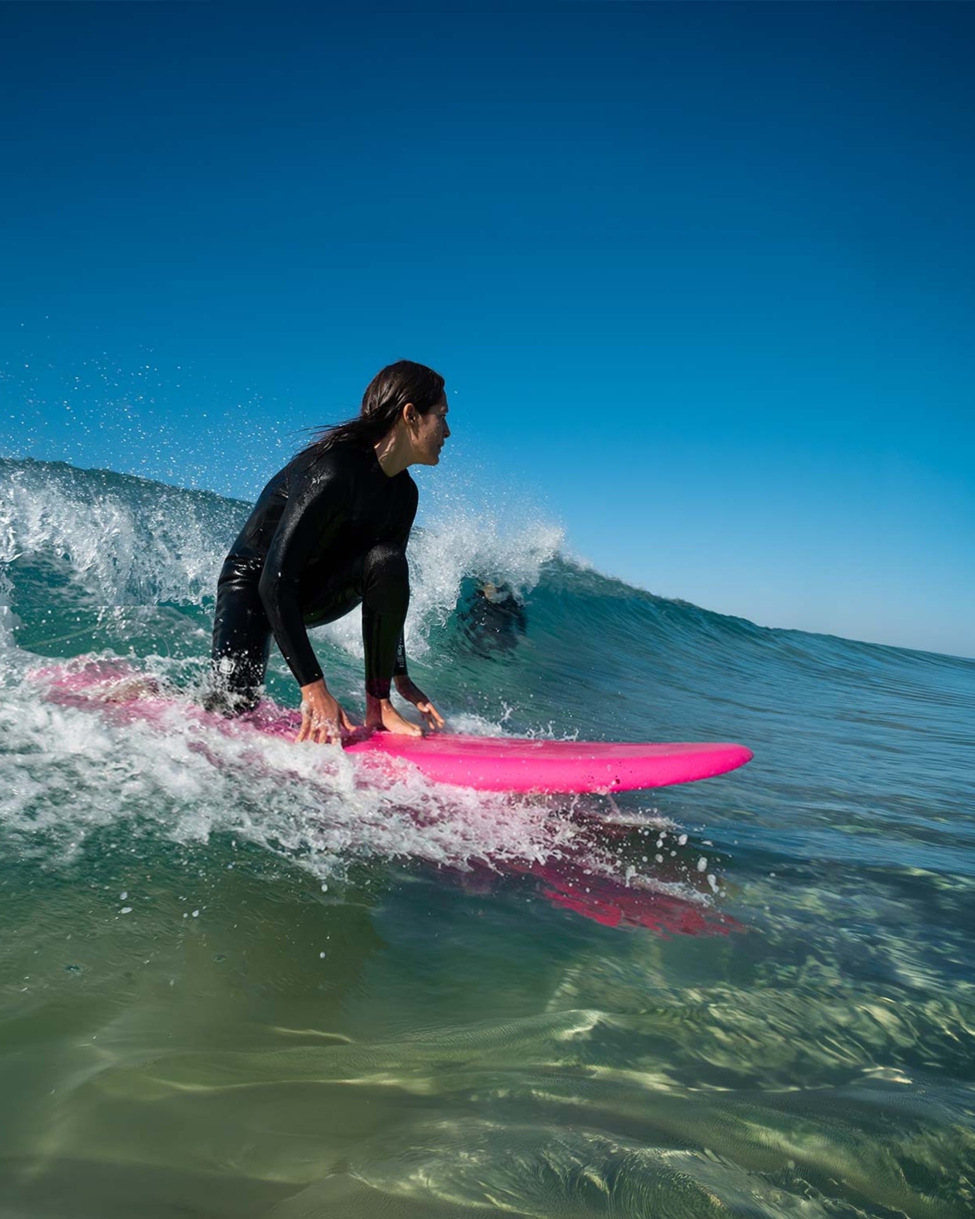 Surfer riding a pink 6'6 surfboard, breaking waves and spray