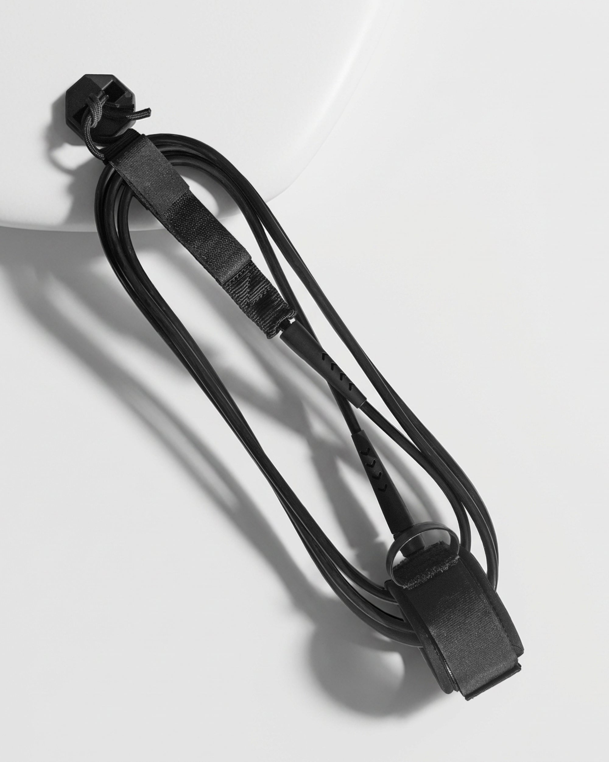 Black surf leash with straps and hook clips, coiled cord close-up
