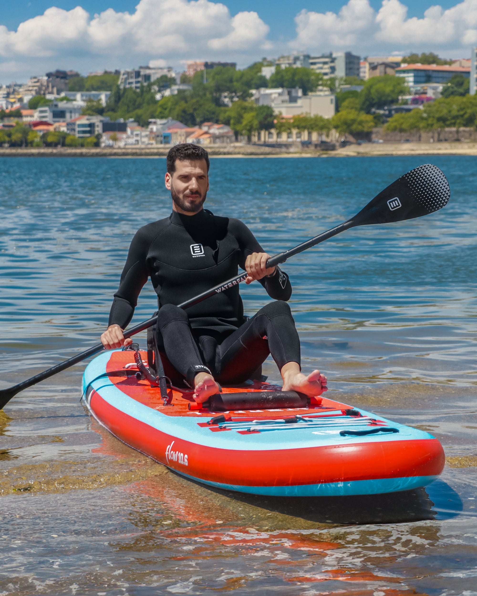 Inflatable SUP with red deck and blue sides, rider holding black paddle